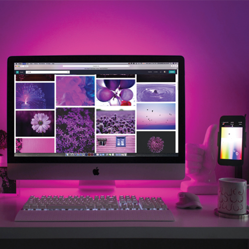 Ordinateur IMAC et téléphone Iphone montrant des photos de fleurs, de ballons et d'eau. Derrière les écrans, le mur reflète violet.