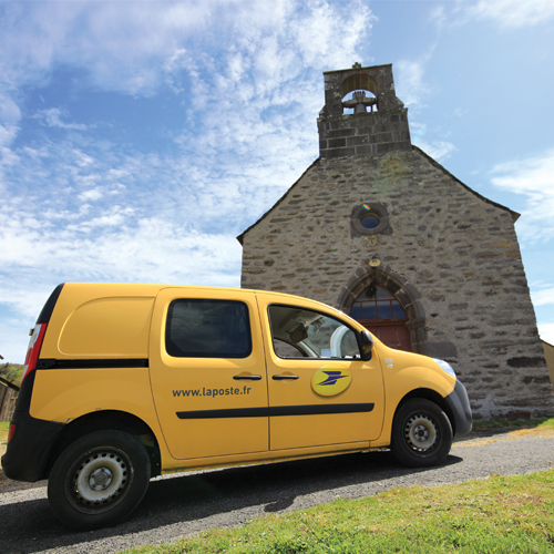 Voiture jaune Kangoo d'un facteur de La Poste en haut d'une colline face à une chapelle