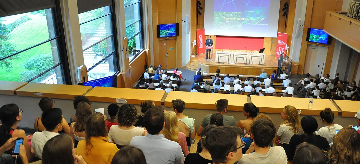 Amphithéatre dans les locaux de Sciences Po où des centaines d'étudiants écoutent leur professeur parler sur son estrade.