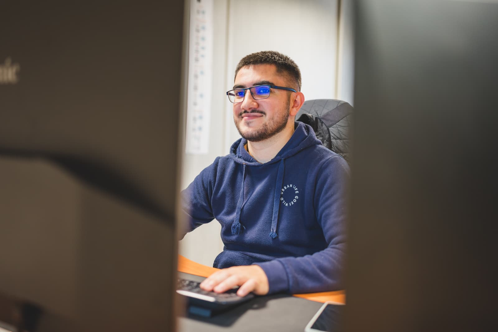 Un homme souriant portant des lunettes est assis devant un ordinateur, travaillant sur le logiciel Ephoto Dam, solution de Digital Asset Management.
