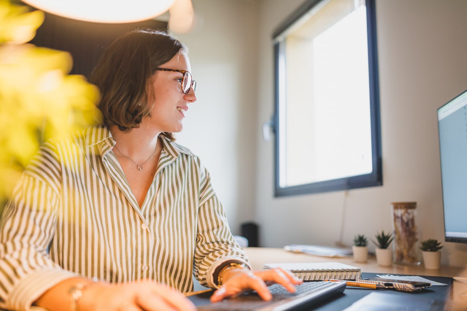 Femme portant des lunettes devant son ordinateur qui regarde son écran et qui tape sur les touches du clavier.