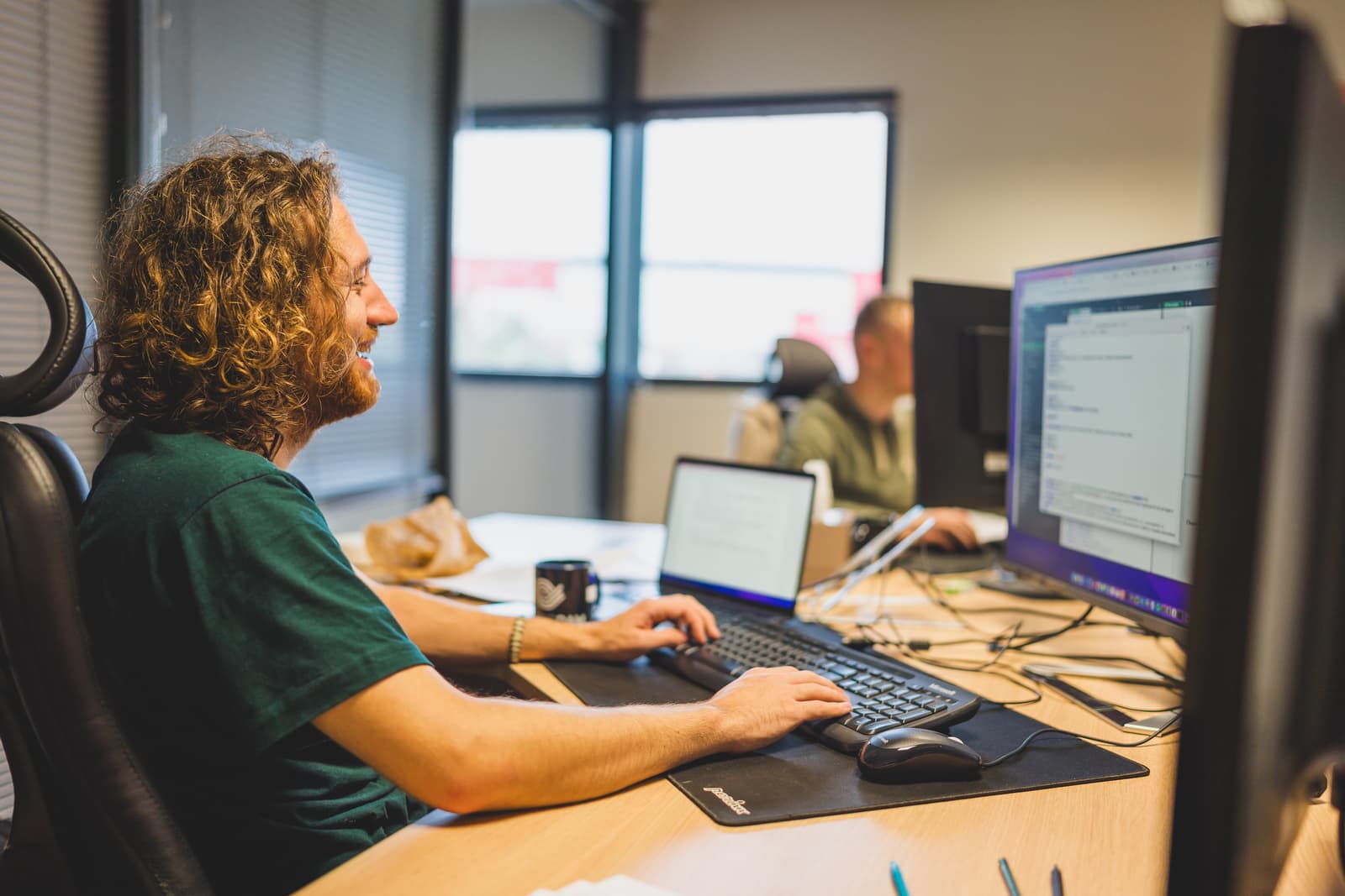 Deux hommes assis à leur bureau devant leur ordinateur en train de sourire, travaillant sur la solution de Digital Asset Managament Ephoto Dam.