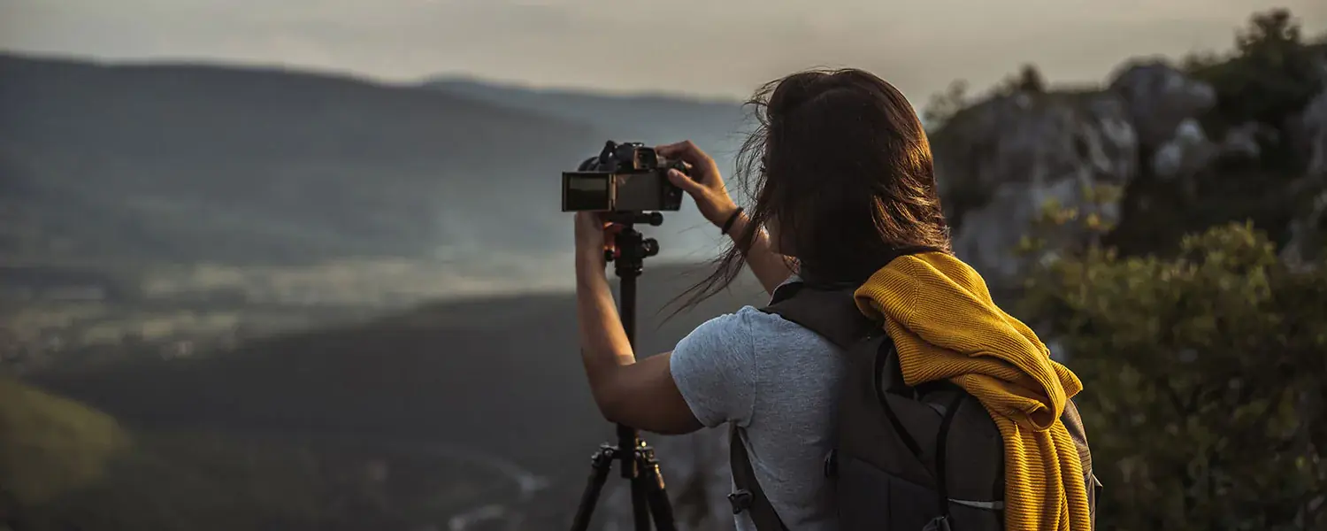 Femme ayant un appareil photo sur trépied dans les mains, prenant une photo du panorama.