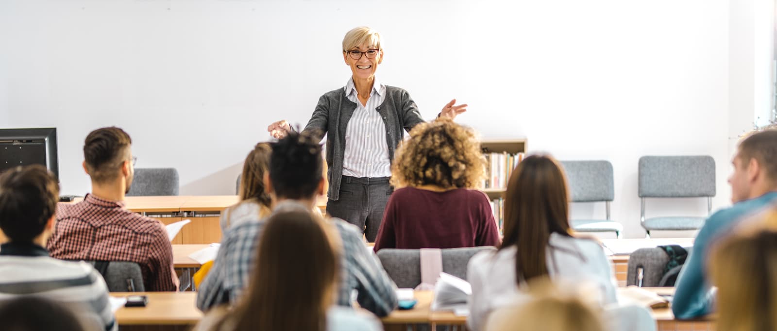 Professeure parlant devant des élèves et qui bouge ses bras pour attirer l'attention.