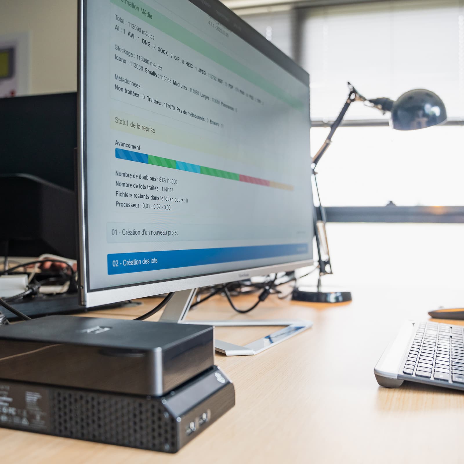 Ordinateur posé sur un bureau avec un clavier, une souri, une lampe et des disques durs.
